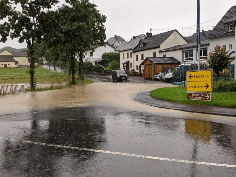 Hochwasser in Kerpen (Eifel), überflutete Straße mit Wegweisern nach Niederehe und Loogh