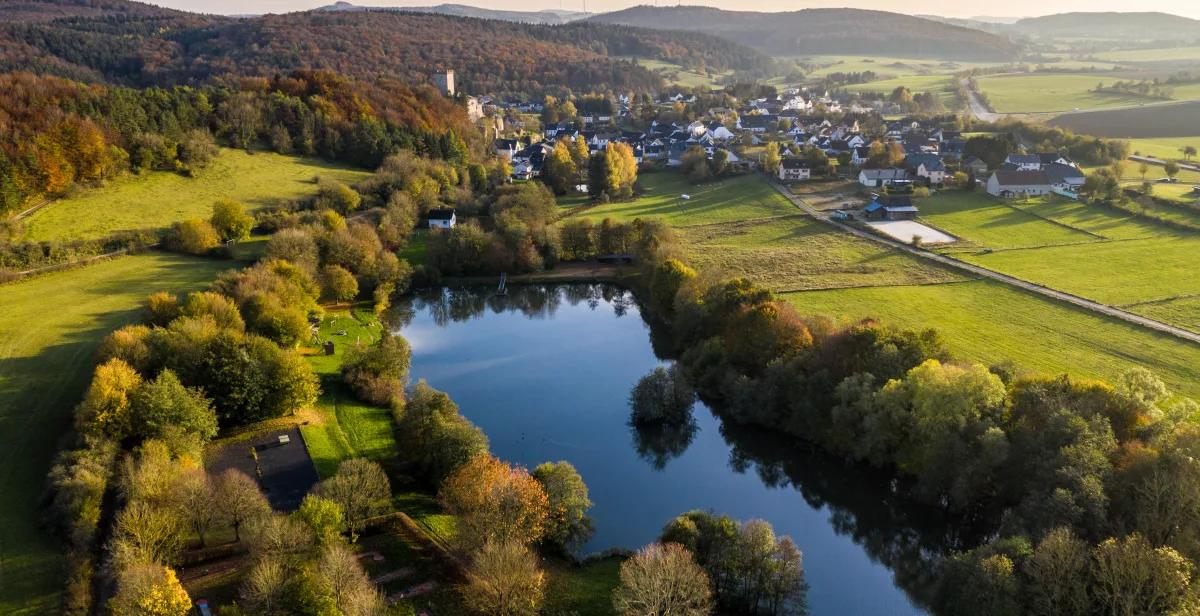 Ruderbach-Stausee Kerpen umgeben von Bäumen mit Blick auf den Ort